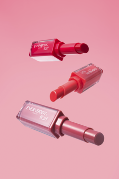 Trzy otwarte pomadki Everybody London x Fluff Strawberry Kiss, w odcieniach czerwieni i różu, unoszące się na różowym tle.