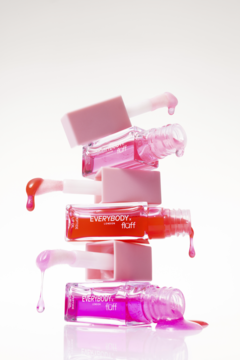 Stos pięciu buteleczek peptydowego olejku Everybody London x Fluff Candy Juice w różu i pomarańczu, z wyciekającym płynem na białym tle.