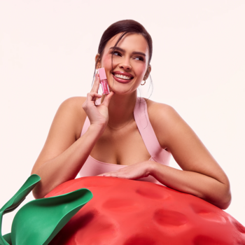 Uśmiechnięta kobieta z olejkiem powiększającym Everybody London x Fluff Candy Juice przy ustach, obok truskawki.