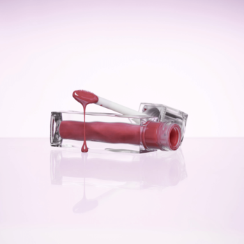 Błyszczyk Muzigae Mansion Icy Glow Petal, otwarty, różowa kropla spływa z aplikatora na tubkę, różowe tło.