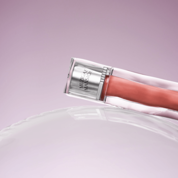 Błyszczyk Muzigae Mansion Icy Glow Better leżący na boku na transparentnym szkle, tło jasnoróżowe.