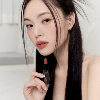 Modelka trzyma otwartą matową pomadkę Muzigae Mansion Prime, sztyft w kolorze brzoskwiniowego beżu.