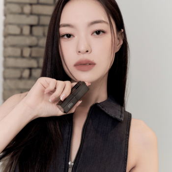 Kobieta trzyma ciemną matową pomadkę Muzigae Mansion Maxi; jej usta w odcieniu nude soft blur, zbliżenie.