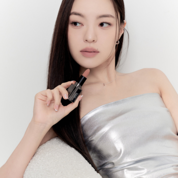 Matowa pomadka Muzigae Mansion Layered w czarnej tubce, z beżowym sztyftem, trzymana przez kobietę. Modelka ma usta w tym odcieniu.