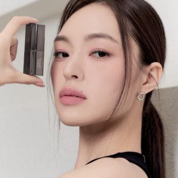 Muzigae Mansion matowa pomadka Babe. Kobieta z efektem soft blur na ustach prezentuje ciemne opakowanie produktu.