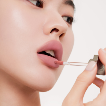 Zbliżenie na kobietę aplikującą matowy tint Muzigae Mansion Poise na usta w kolorze zgaszonego różu, z gładkim, aksamitnym wykończeniem.