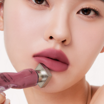 Matowy tint Muzigae Mansion Symbol w odcieniu śliwkowym na ustach kobiety, aplikowany z tubki. Bliskie ujęcie.