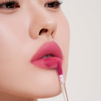 Zbliżenie na usta; aplikator nakłada żelowy tint Muzigae Mansion Knockout w odcieniu głębokiego różu, z matowym wykończeniem.