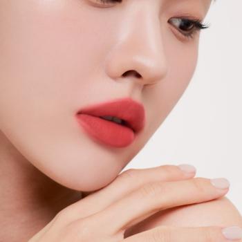 Zbliżenie na usta kobiety z matowym tintem Muzigae Mansion w odcieniu Pleasure, o ciepłym, koralowym kolorze.