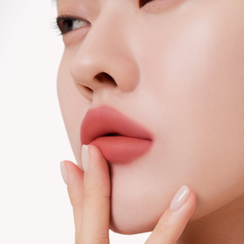 Muzigae Mansion Tint Melted, matowe usta w kolorze terakoty. Kobieta dotyka brody dłonią.