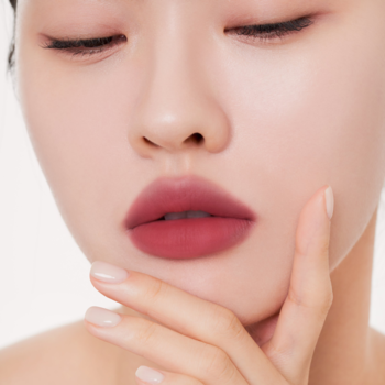 Zbliżenie na usta kobiety z matowym, czerwonobrązowym tintem Muzigae Mansion Pairing, dłoń przy podbródku.