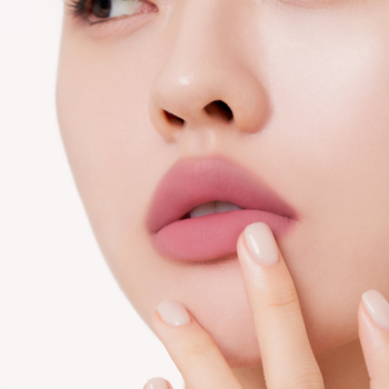 Usta z matowym tintem Muzigae Mansion Dawn Rose. Palec dotyka wargi, podkreślając miękkie wykończenie.