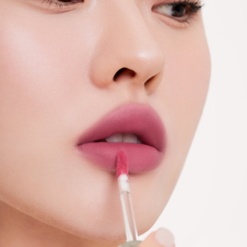 Zbliżenie ust z aplikatorem. Kobieta nakłada różowy, matowy tint Muzigae Mansion Gypsy Rose z efektem rozmycia.