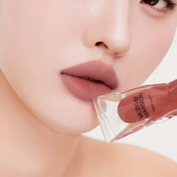 Usta pomalowane matowym tintem Muzigae Mansion Mania, obok przezroczyste opakowanie produktu.