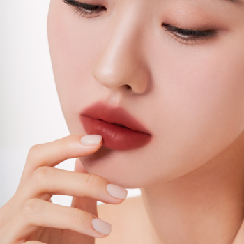 Zbliżenie na usta z matowym tintem Muzigae Mansion Chillin w odcieniu rdzawego brązu, z dłonią.