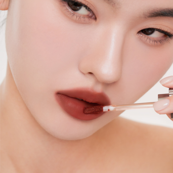 Kobieta aplikuje lekki tint do ust Muzigae Mansion Undone, matowy, brązowo-czerwony kolor na usta.