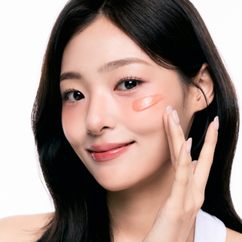 Kobieta nakładająca brzoskwiniowy róż w kremie na policzek, dla uzyskania świeżego, naturalnego blasku cery.