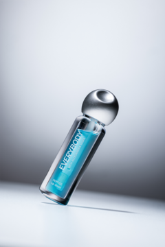 Błyszczyk Cold me z niebieskim płynem, przezroczysta butelka z napisem EVERYBODY, srebrna nakrętka, widok pod kątem.