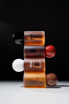 Mgiełki do ciała i włosów mnj, cztery bursztynowe butelki z kolorowymi zakrętkami, pionowo na ciemnym tle.