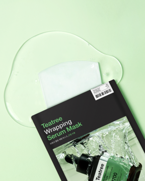 Teatree Wrapping Serum Mask w czarnym opakowaniu, butelka z drzewem herbacianym, serum na jasnozielonym tle.