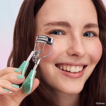 Uśmiechnięta kobieta trzyma srebrną zalotkę z brokatową turkusową rączką blisko oka. Ma turkusowe paznokcie.