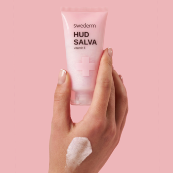 Różowa tubka Swederm HUD SALVA vitamin e w dłoni, z widoczną perłową konsystencją maści na skórze.