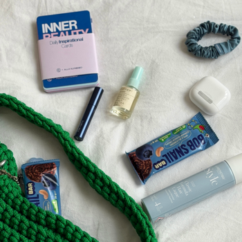 Codzienne akcesoria na białym tle: zielona pleciona torba, białe słuchawki, karty, przekąski, perfumy i spray Dove Style + Care.