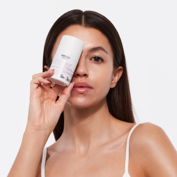 Biała tuba Veoli Botanica But First Sunscreen SPF 50+ w dłoni kobiety przy twarzy. Nawilżający krem ochronny.