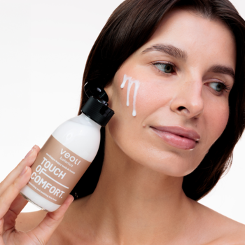 Kobieta nakłada nawilżający tonik Veoli Botanica Touch Of Comfort na policzek, z butelki spływa biały płyn.