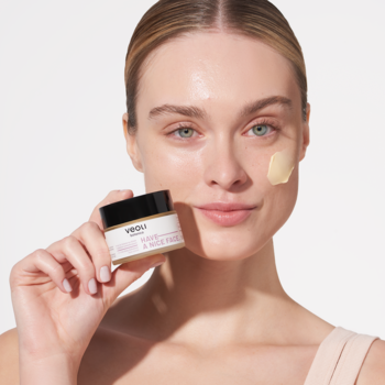 Kobieta aplikuje nawadniający krem Veoli Botanica Have a Nice Face na twarz, trzymając otwarty słoiczek z żółtym kremem.