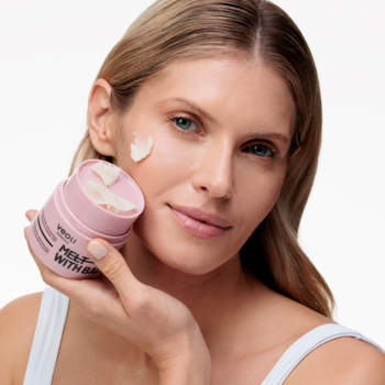 Kobieta nakłada różowe masełko Veoli Botanica Melt With Balance do demakijażu i SPF z różowego słoiczka na policzek.