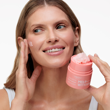 Kobieta aplikuje łagodzące masełko Veoli Botanica Melt With Kindness do demakijażu, różowy słoik w dłoni.