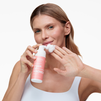 Kobieta aplikuje łagodzącą piankę Veoli Botanica Foam Of Kindness na dłoń, różowo-biała butelka.