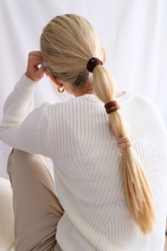 Kobieta tyłem, długi blond kucyk bubble ponytail spięty trzema neutralnymi gumkami do włosów. Biały sweter.