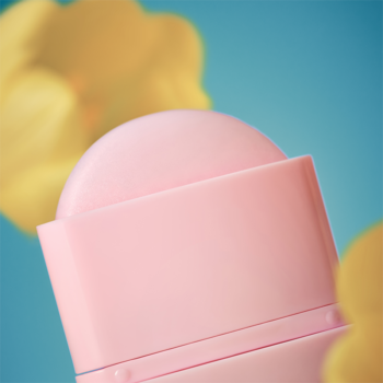 Zbliżenie na otwarty różowy balsam w sztyfcie z zaokrąglonym aplikatorem, na turkusowym tle z żółtymi kwiatami.