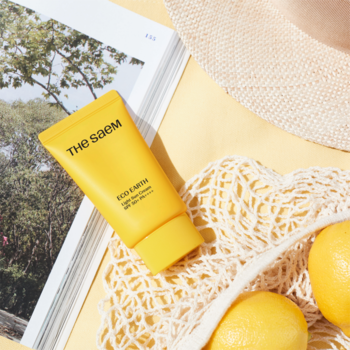 Żółta tuba kremu przeciwsłonecznego The Saem Eco Earth Power Pink Sun Cream SPF50+ na magazynie z cytrynami i kapeluszem, widok z góry.