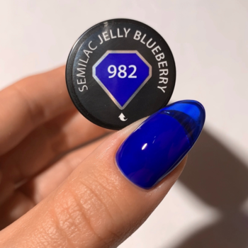 Zbliżenie: dłoń trzyma zakrętkę lakieru Semilac Jelly Blueberry 982 i paznokieć w głębokim, półprzezroczystym błękicie.