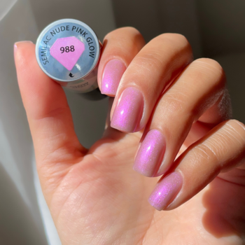Dłoń z błyszczącymi, różowo-beżowymi paznokciami Semilac 988 Nude Pink Glow, trzyma butelkę lakieru hybrydowego.