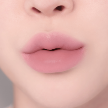 Zbliżenie na matową, pudrowo-różową pomadkę na pełnych ustach, delikatnie wydętych w dzióbek.