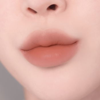 Zbliżenie na pełne usta z matową pomadką w odcieniu brzoskwiniowego różu, z efektem ombre, widok z przodu.