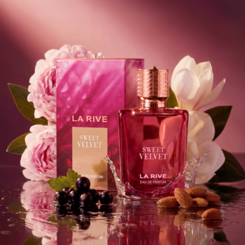 LA RIVE SWEET VELVET Eau de Parfum. Różowa butelka i pudełko wśród piwonii, czarnych porzeczek i migdałów. Różowe tło.