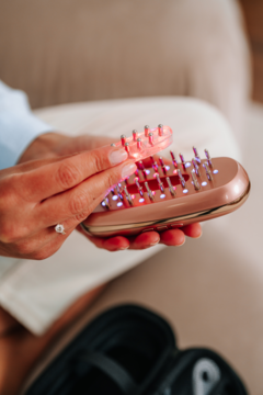 Zbliżenie na różowo-złoty grzebień Beautifly LaserBoost Pro z czerwonymi światłami, trzymany w dłoniach.