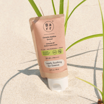 Kojąca esencja Barr Centella SPF 50+ PA++++ w jasnoróżowej tubce na piasku, na tle zielonych traw.