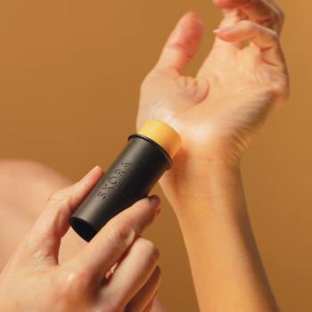 Dłoń aplikuje czarny balsam regenerujący w sztyfcie na skórę nadgarstka, nawilżając suchą skórę.