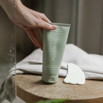 Polemika Multifunkcyjny balsam wygładzająco-kojący w jasnozielonej tubie, w dłoni, obok biały gua sha.