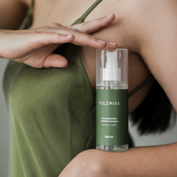 Kobieta w zielonym topie trzyma butelkę Antyoksydacyjnej mgiełki tonizującej Polemika 100 ml z atomizerem.