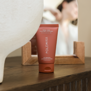 Polemika Peeling-Maska enzymatyczna w terakotowej tubie na drewnianej komodzie, kobieta w lustrze.