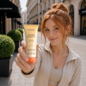Kobieta prezentuje żółto-pomarańczowy krem do rąk Hand Screen SPF 50. Widok z przodu na tle ulicy.