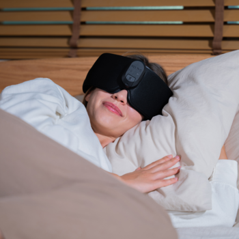 Kobieta nosi czarną podgrzewaną maskę do spania RENPHO EyeSnooze Aroma, leżąc zrelaksowana w łóżku.