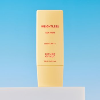 Jasnożółta butelka HOUSE OF HUT WEIGHTLESS Sun Fluid SPF50+ PA++++, widok z przodu, na tle błękitnego nieba.